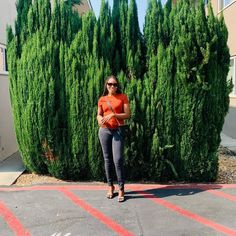 a woman is standing in front of some trees and bushes with her hand on her hip