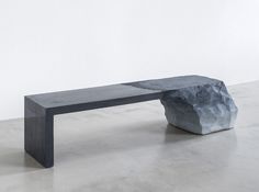 a stone bench sitting on top of a cement floor next to a white wall in an empty room