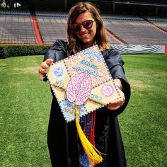 a woman in graduation gown holding up a piece of paper with a brain on it