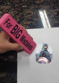 a hand holding a pink eraser next to a piece of paper with an image of captain america on it