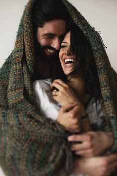 a man and woman wrapped in a blanket smiling at each other with their eyes closed