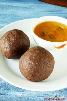 two balls of food on a white plate with a bowl of soup in the background