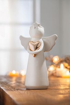 a white angel figurine with a gold heart on it's chest sitting on a wooden table