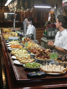 several people standing at a buffet line with food on plates and serving utensils