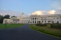 a large white building sitting on the side of a road next to a lush green field