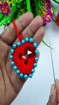 a person holding a pair of scissors near a red beaded heart ornament