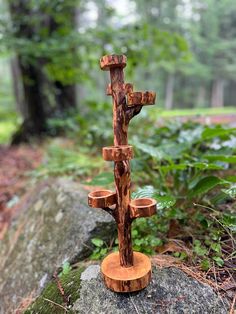 a wooden cross sitting on top of a rock in the woods