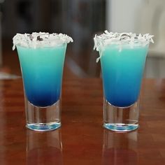 two glasses filled with blue liquid on top of a wooden table