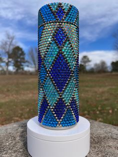 a blue and green vase sitting on top of a white pedestal next to a field