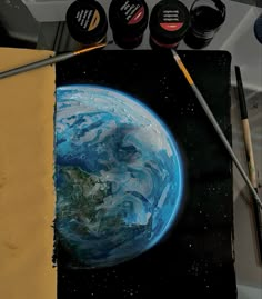 an artist's painting of the earth with paintbrushes next to it