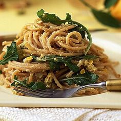 a white plate topped with pasta and greens on top of a table next to a fork