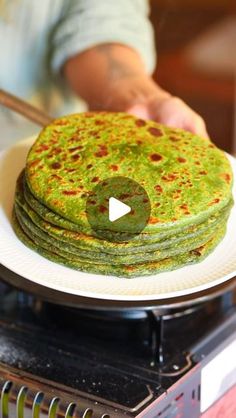 a stack of green pancakes sitting on top of a white plate next to a frying pan