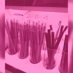 several cups filled with different types of pens and pencils sitting on a table next to each other