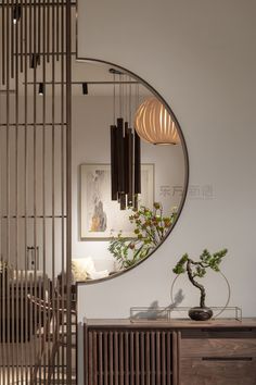 a round mirror hanging on the wall above a wooden dresser and vase with flowers in it