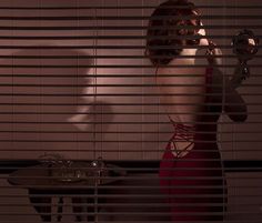 a woman in a red dress standing behind blinds