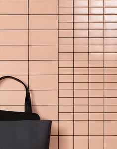 a black handbag sitting on top of a pink tiled wall next to a purse