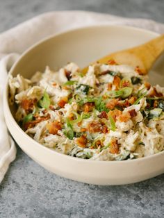 a white bowl filled with food on top of a gray counter next to a wooden spoon