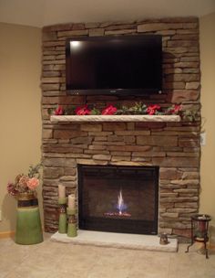 a stone fireplace with a flat screen tv above it and flowers on the mantle below