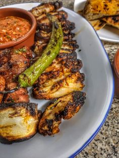 a plate full of grilled meat and vegetables with dipping sauces on the side