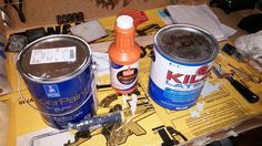 two paint cans sitting on top of a table next to other paints and tools in a box