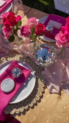 the table is set with pink napkins, plates and vases filled with roses