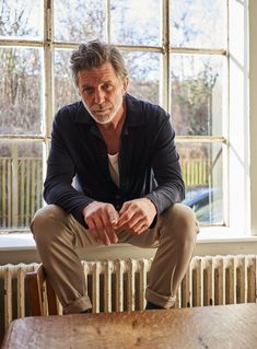 a man sitting on top of a wooden table next to a radiator in front of a window