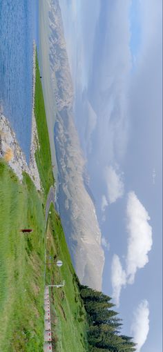 an aerial view of a road near the ocean and mountains with clouds in the sky