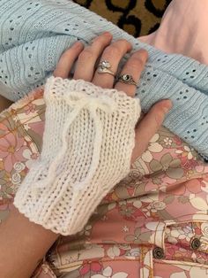 a woman wearing white knitted gloves and holding her hand in the other direction with two rings on it