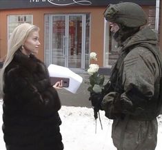 a man in winter clothes standing next to a woman holding a box with flowers on it