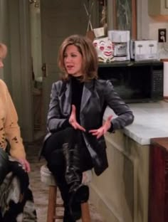 two women sitting on stools talking to each other in front of a kitchen counter