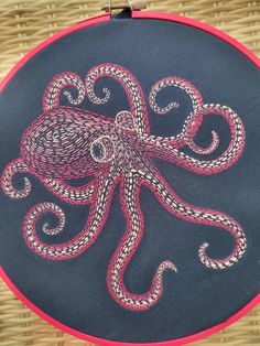 an embroidered octopus on a black and pink circular piece of cloth with red piping