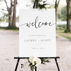 a welcome sign with flowers and greenery sits on an easel in front of trees