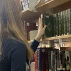 a woman is reaching for a book on a shelf in a library with many books