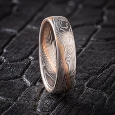 "* Price may vary depending on ring size, please inquire with us directly with your needed size for accurate pricing! This Mokume Gane ring is shown in the Twist pattern and Smoke Palette, with a low dome profile and satin finish. This design has two beautiful stratum layers added in, one red gold and one gold, side by side with a layer of silver in between, creating a pop of color and warmth to contrast with the silvery cool look of the Ash palette. The Ash palette features palladium and sterling silver. Pattern: Twist Palette: Ash Finish: Satin Profile: Low Dome  Width Shown: 5.5mm Size Shown: 9.25 Add On: Red Gold Stratum and Yellow Gold Stratum We care about customer service and would like to hear from you! Please contact us to help create your treasured item, we take your concerns and Round Patina Rings For Anniversary, Minimalist Etched Round Ring, Modern Etched Rings, Mokume Gane Ring, Twist Pattern, Mokume Gane, Men's Jewelry, Side By Side, Silver Band