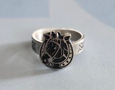 This ring was designed with the horse in a horseshoe symbol. The beautiful pewter ring is a silver color and the background is blackened to bring out the fine detail of the design. Our rings are 100% Lead and nickel free pewter and made in the USA The top design part of the ring measures approx. 12.5mm x 11.5mm  The ring band tapers from about 5mm to about 4mm at the bottom and is about 1.5mm thick Picture shows size compared to a US Dime Rings are available in sizes 4 to 7 (half sizes also) Silver Horseshoe Ring As Gift, Silver Horseshoe Ring For Gift, Silver Adjustable Horseshoe Rings, Pewter Ring, Ladies Ring, Top Design, The Horse, Ring Band, Rings Statement