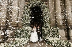 a bride and groom standing in front of a building surrounded by white flowers