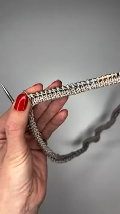 a woman is holding a crochet hook with red nail polish on her nails