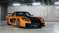 an orange and black sports car parked in a parking garage next to a wall with lights on