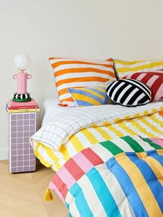 a bed with colorful sheets and pillows on top of it next to a night stand