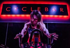 a woman on a stationary bike in front of a neon sign that reads cyclebar