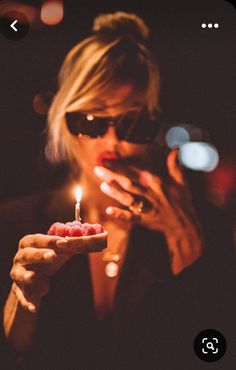 a woman holding a small piece of food in her hand with a lit candle on it