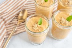 four small jars filled with smoothie on top of a white tablecloth next to spoons