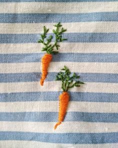 two small carrots are embroidered onto a blue and white striped fabric surface, with green leaves on top