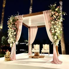 an outdoor wedding setup with white chairs and pink draping on the stage at night