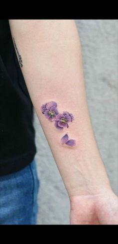 a woman's arm with three purple flowers on the left side of her wrist