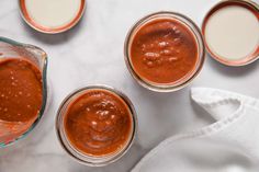 three jars filled with sauce sitting on top of a counter next to two napkins