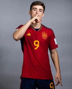 a soccer player poses for a portrait with his finger in his mouth while wearing a red jersey