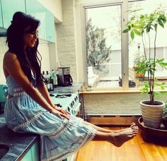 a woman sitting on top of a kitchen counter next to a potted plant in front of a window