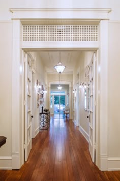 an empty hallway with wooden floors and white trim on the walls, leading to another room