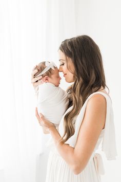 a woman holding a baby in her arms and kissing it's face with the other hand